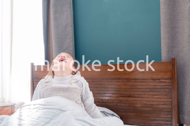 朝ベッドで目覚めて伸びをする小さな女の子