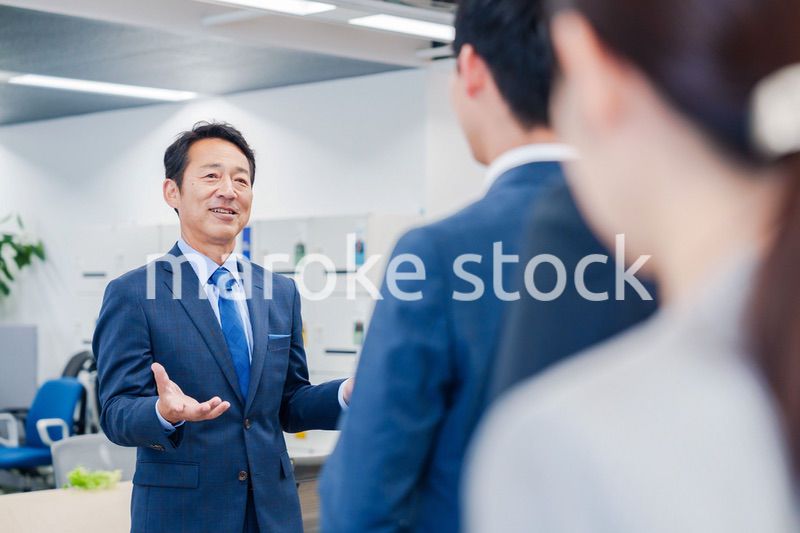 オフィスでの朝礼で挨拶をする管理職の男性