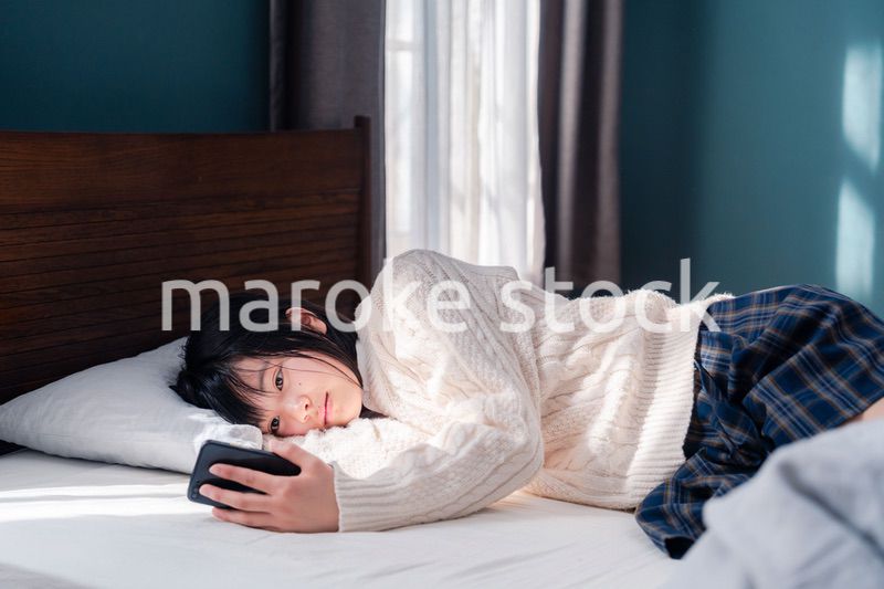ベッドに寝転がってスマホを使う思春期の少女