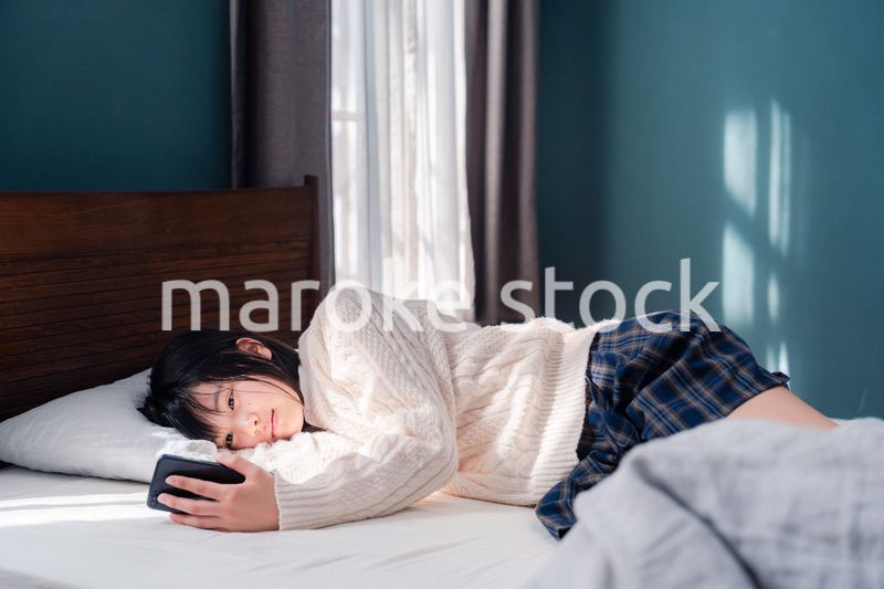 ベッドに寝転がってスマホを使う思春期の少女