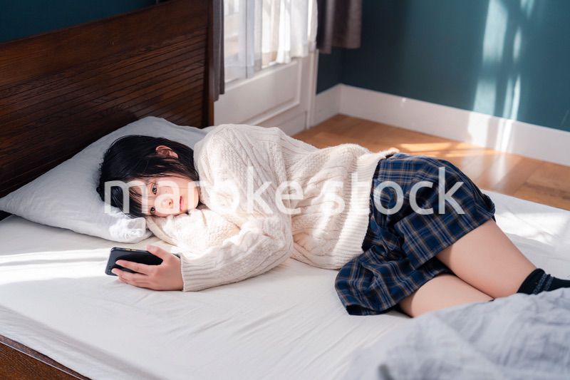 ベッドに寝転がってスマホを使う思春期の少女