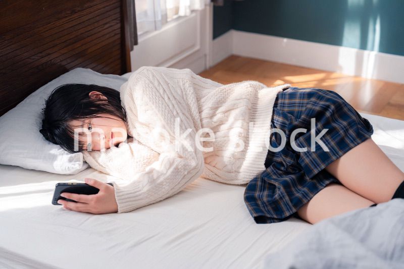 ベッドに寝転がってスマホを使う思春期の少女