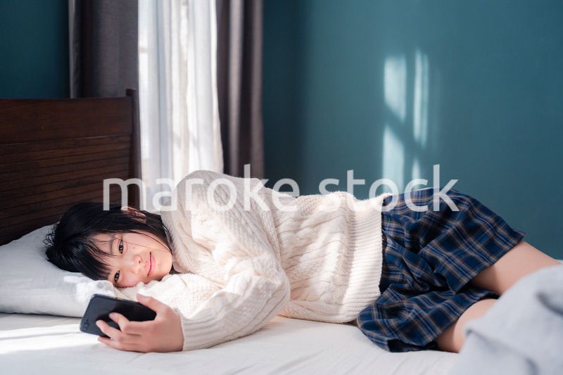 ベッドに寝転がってスマホを使う思春期の少女