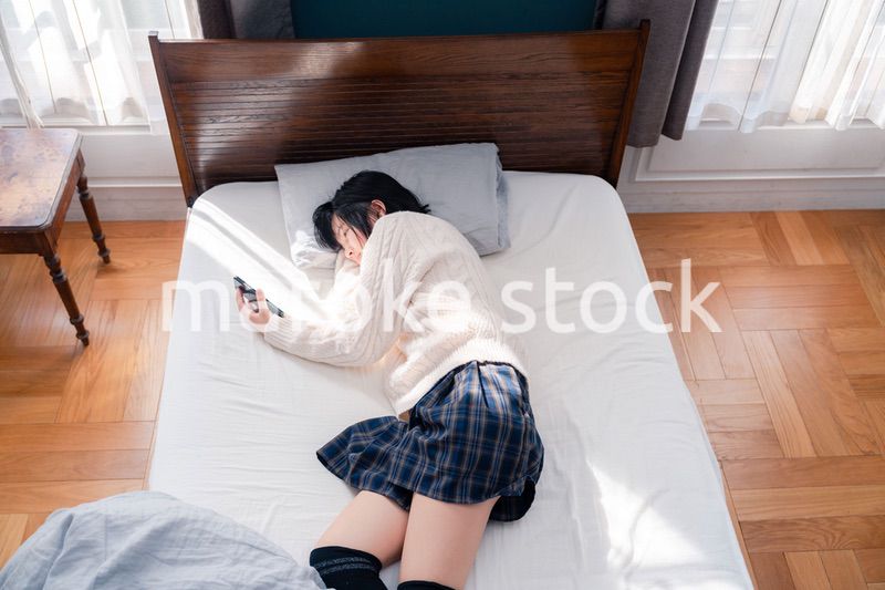 ベッドに寝転がってスマホを使う思春期の少女