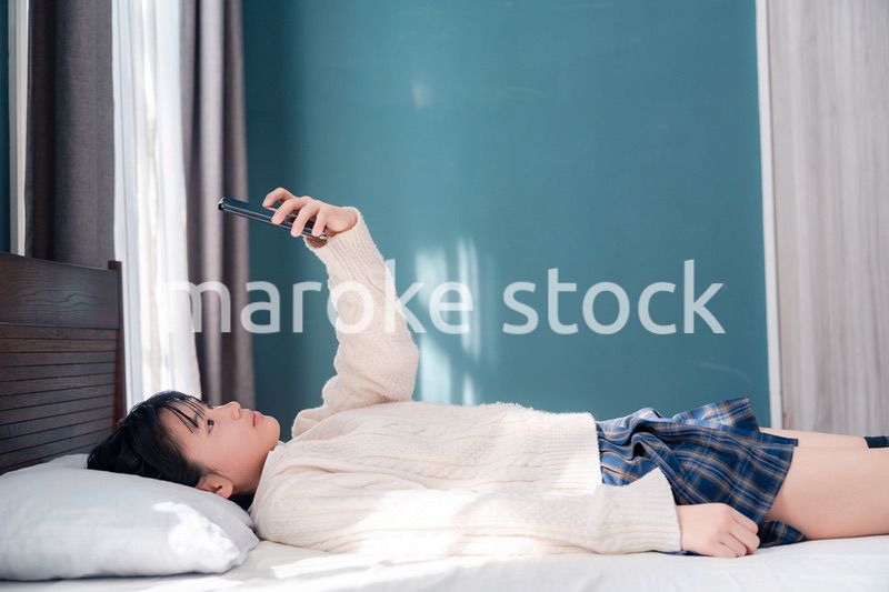 ベッドに寝転がってスマホを使う思春期の少女