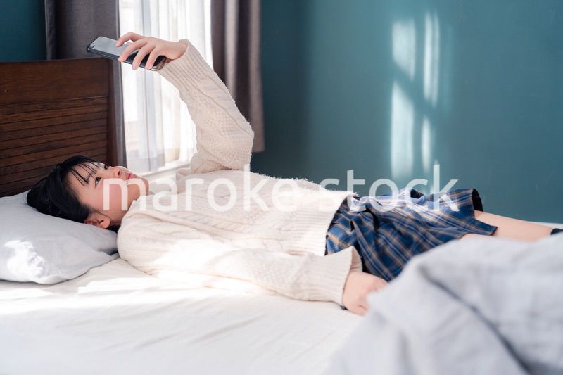 ベッドに寝転がってスマホを使う思春期の少女