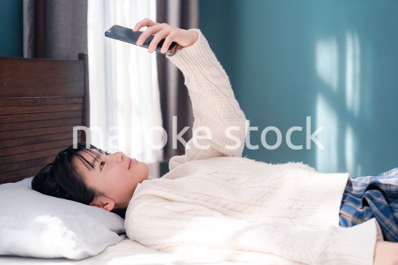 ベッドに寝転がってスマホを使う思春期の少女