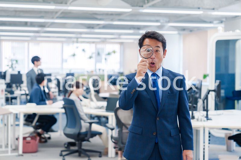 オフィスで虫眼鏡を使う中年のビジネスマン
