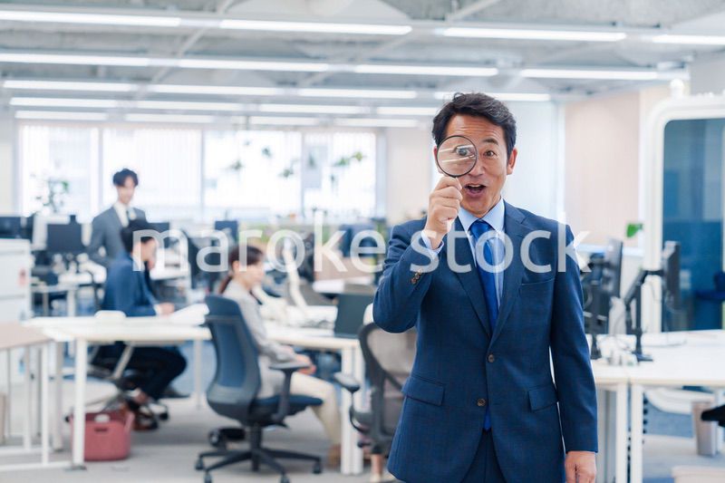 オフィスで虫眼鏡を使う中年のビジネスマン