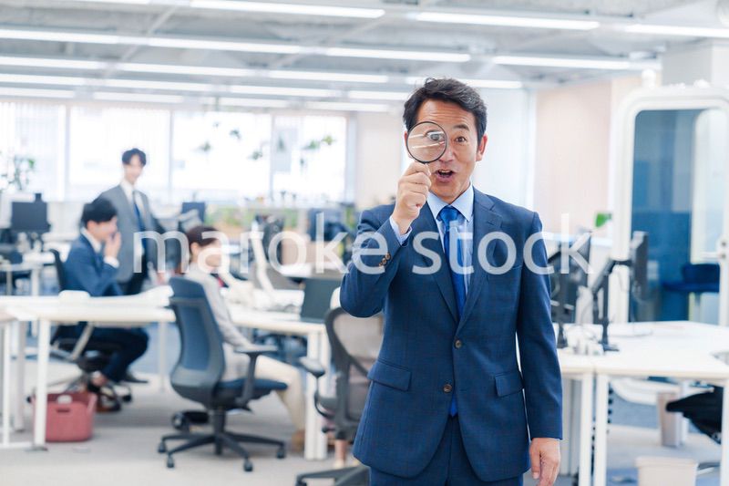 オフィスで虫眼鏡を使う中年のビジネスマン