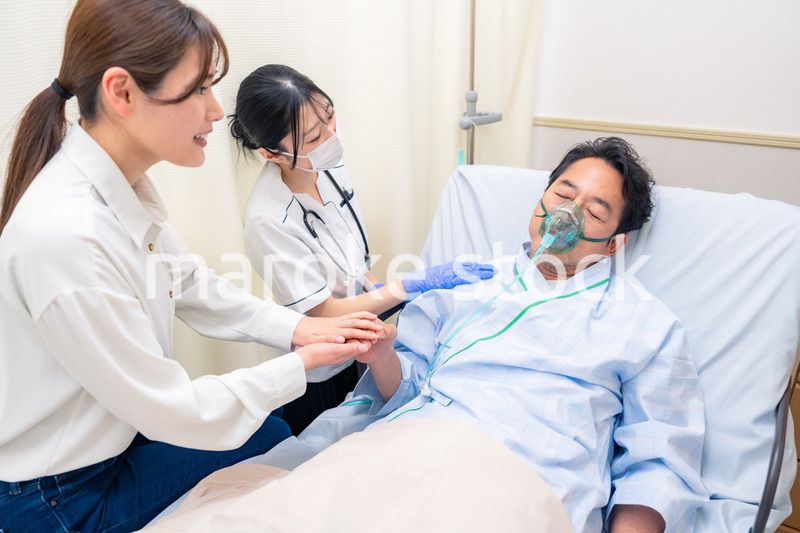 人工呼吸器をつけた家族のお見舞いをする若い女性