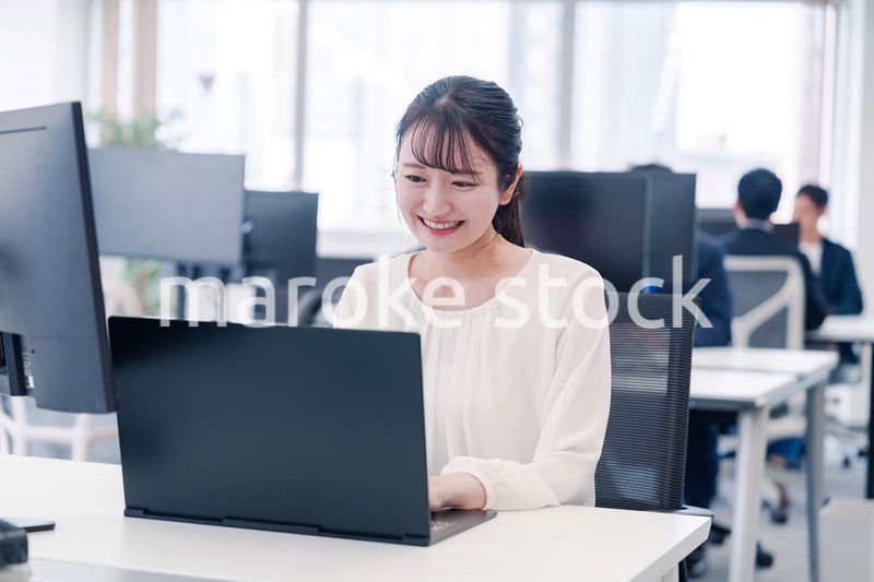 オフィスで笑顔でデスクワークをする若い女性