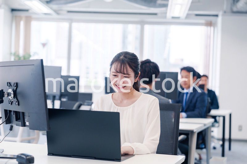 オフィスで笑顔でデスクワークをする若い女性