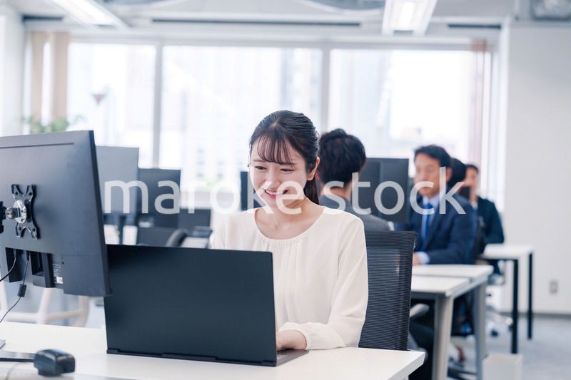 オフィスで笑顔でデスクワークをする若い女性