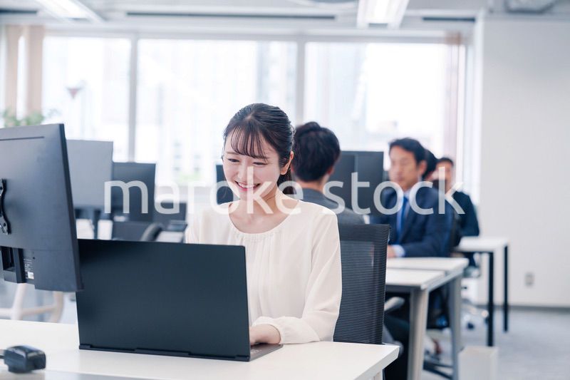 オフィスで笑顔でデスクワークをする若い女性
