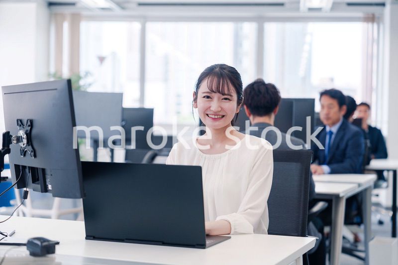 オフィスで笑顔でデスクワークをする若い女性