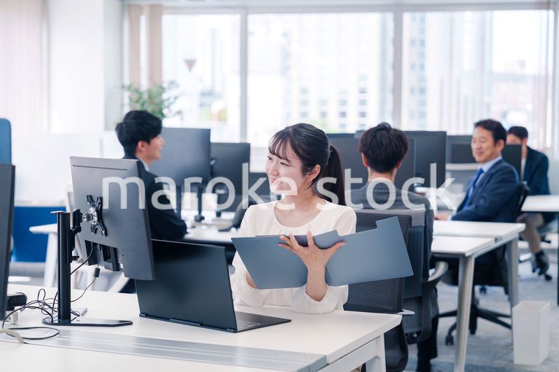 オフィスで笑顔でデスクワークをする若い女性