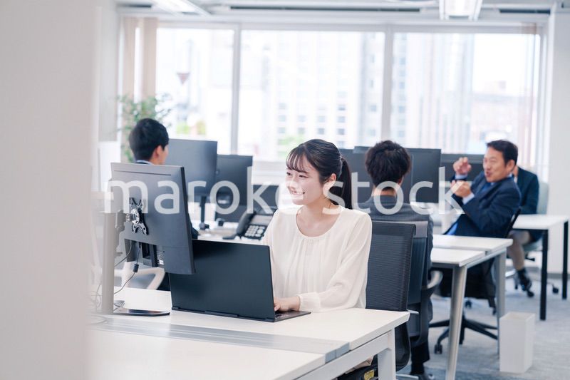 オフィスで笑顔でデスクワークをする若い女性