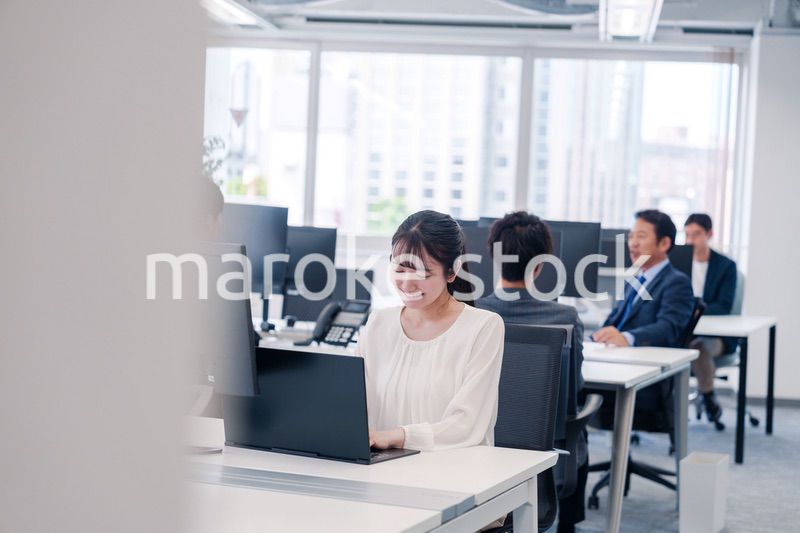 オフィスで笑顔でデスクワークをする若い女性