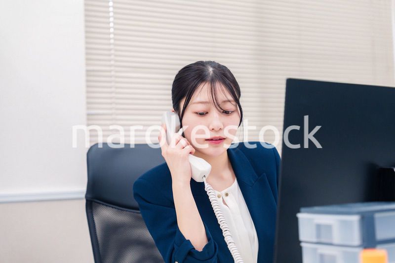 オフィスの固定電話で通話をする女性ビジネスパーソン