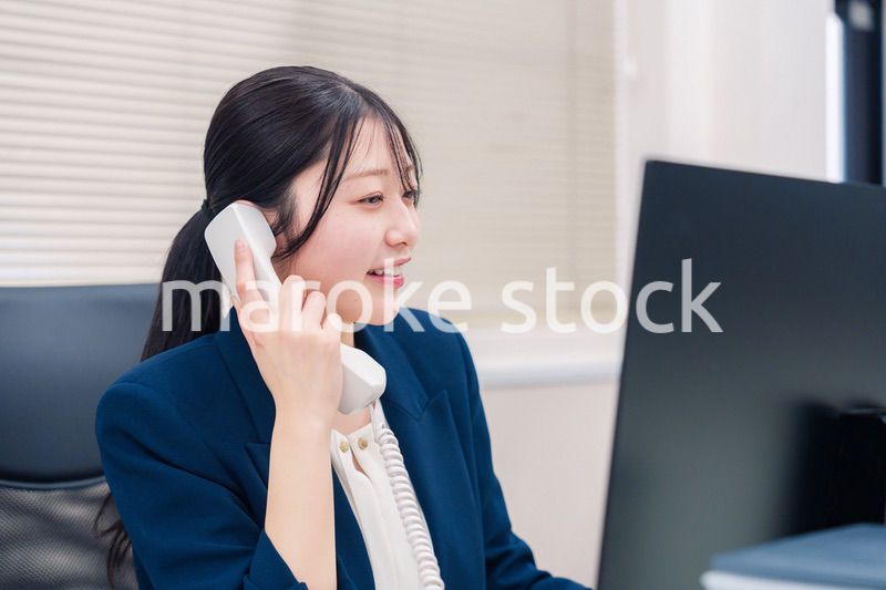 オフィスの固定電話で通話をする女性ビジネスパーソン