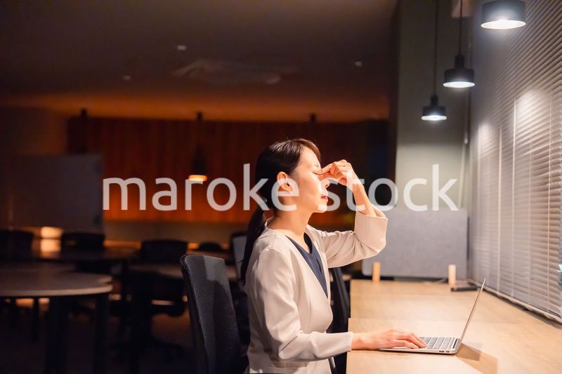 オフィスで暗くなるまで残業をして疲れる女性管理職