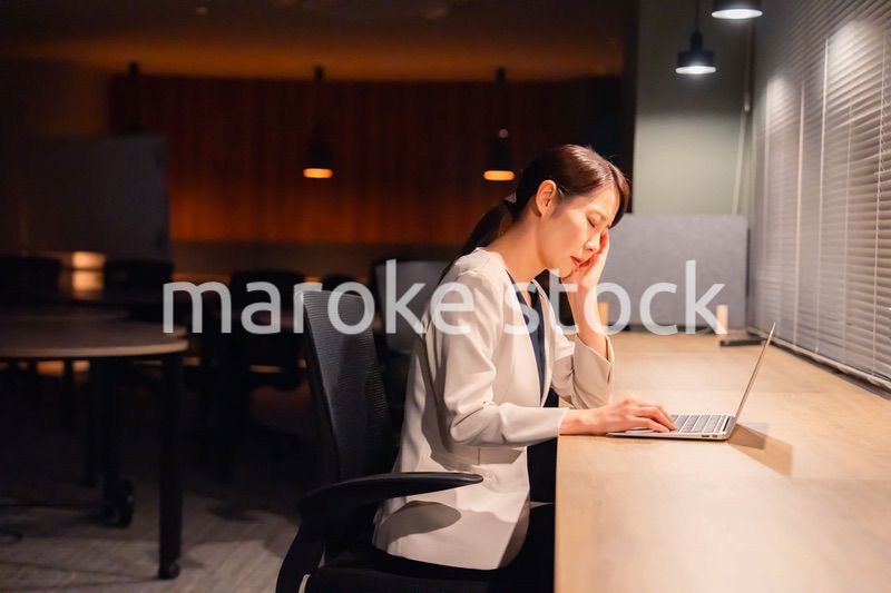 オフィスで暗くなるまで残業をして疲れる女性管理職