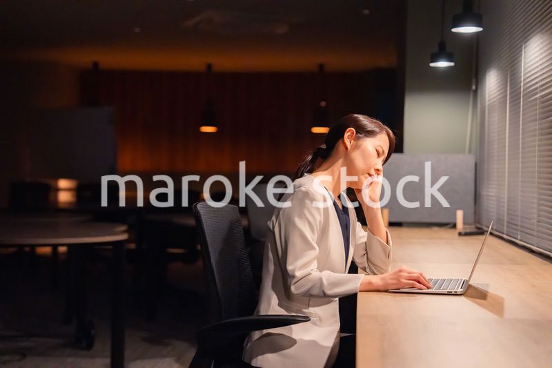 オフィスで暗くなるまで残業をして疲れる女性管理職