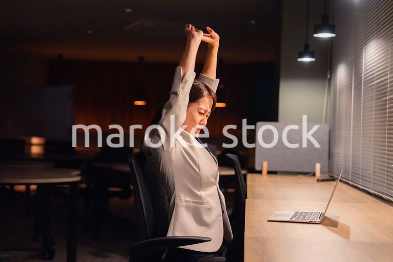 オフィスで暗くなるまで残業をして疲れる女性管理職