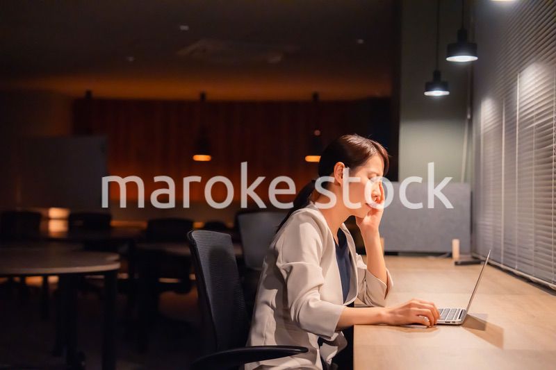 オフィスで暗くなるまで残業をして疲れる女性管理職