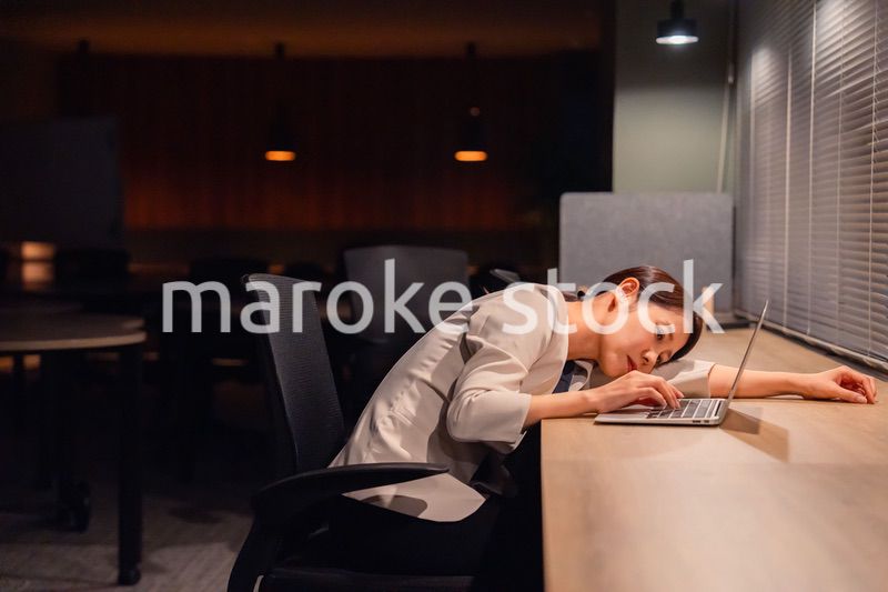 オフィスで暗くなるまで残業をして疲れる女性管理職