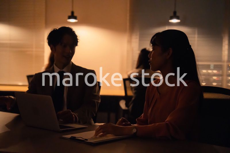 多忙で照明が消えたあとも仕事をする男女のビジネスパーソン