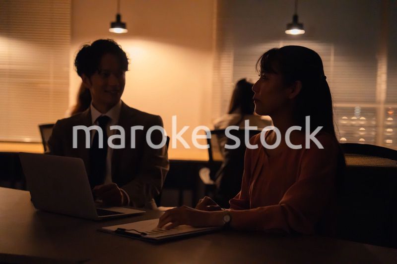 多忙で照明が消えたあとも仕事をする男女のビジネスパーソン