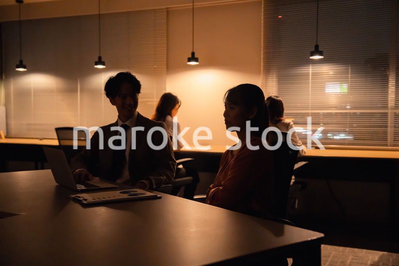 多忙で照明が消えたあとも仕事をする男女のビジネスパーソン