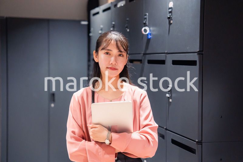 オフィスのロッカーの前でパソコンを持つ若い女性