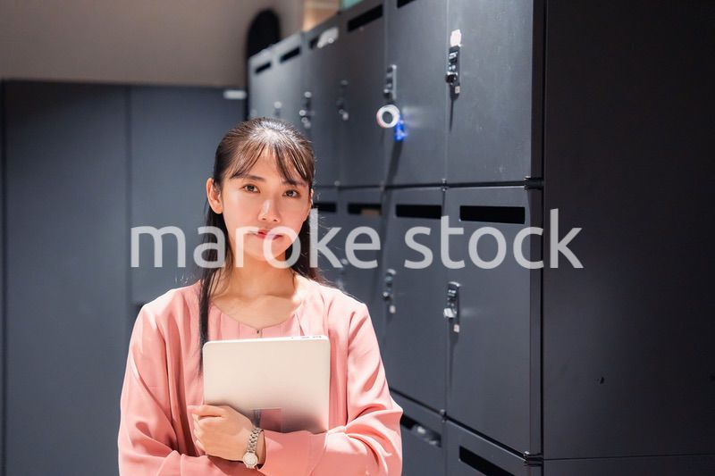 オフィスのロッカーの前でパソコンを持つ若い女性