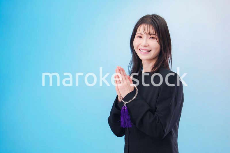 喪服を着て手を合わせる女性（水色背景）