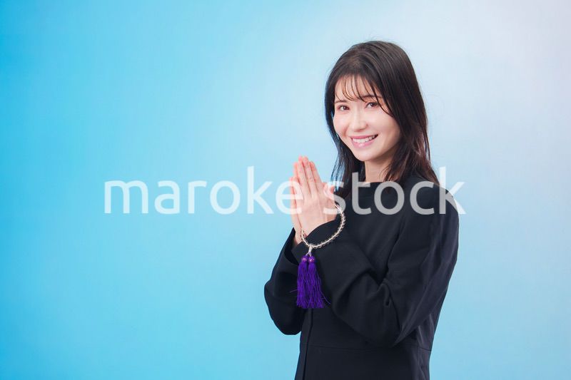 喪服を着て手を合わせる女性（水色背景）