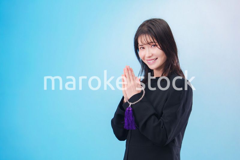 喪服を着て手を合わせる女性（水色背景）