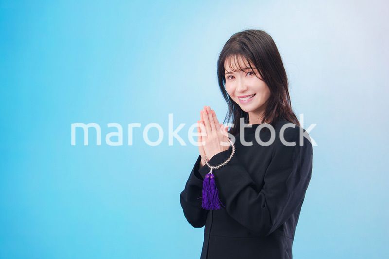 喪服を着て手を合わせる女性（水色背景）