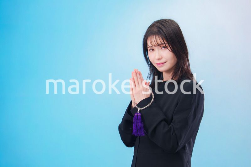 喪服を着て手を合わせる女性（水色背景）