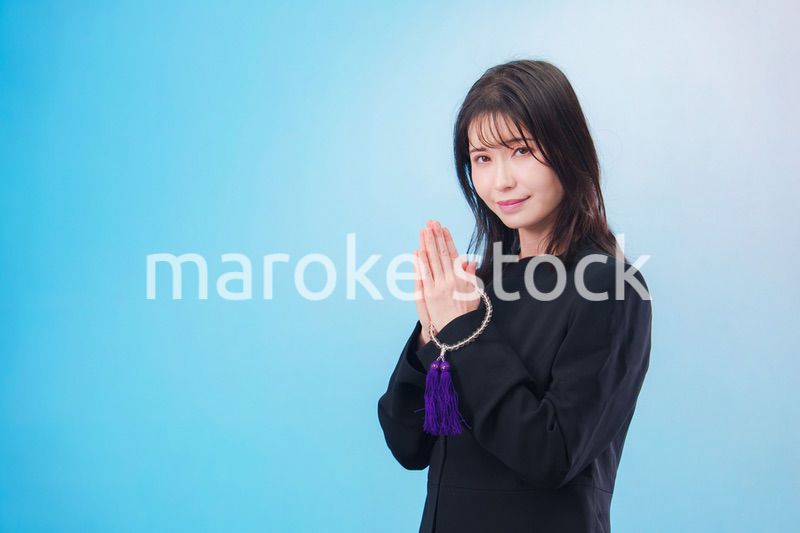 喪服を着て手を合わせる女性（水色背景）