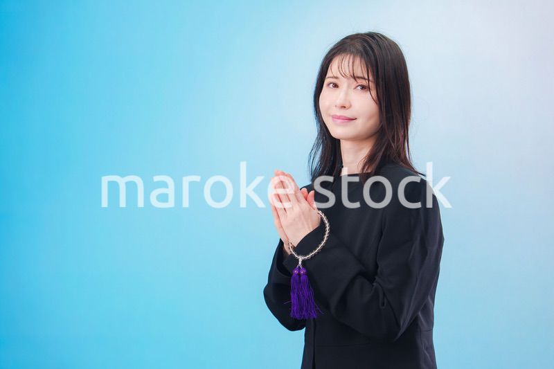 喪服を着て手を合わせる女性（水色背景）