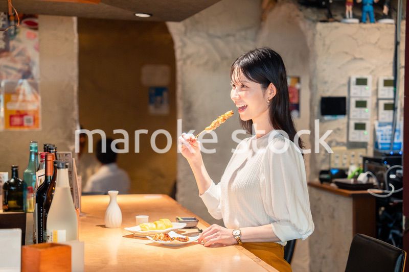 一人でカウンター席に座って焼き鳥を食べる女性