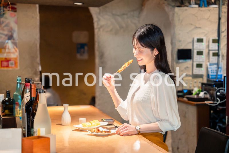一人でカウンター席に座って焼き鳥を食べる女性