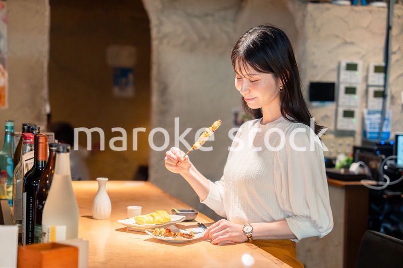 一人でカウンター席に座って焼き鳥を食べる女性