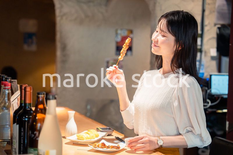 一人でカウンター席に座って焼き鳥を食べる女性