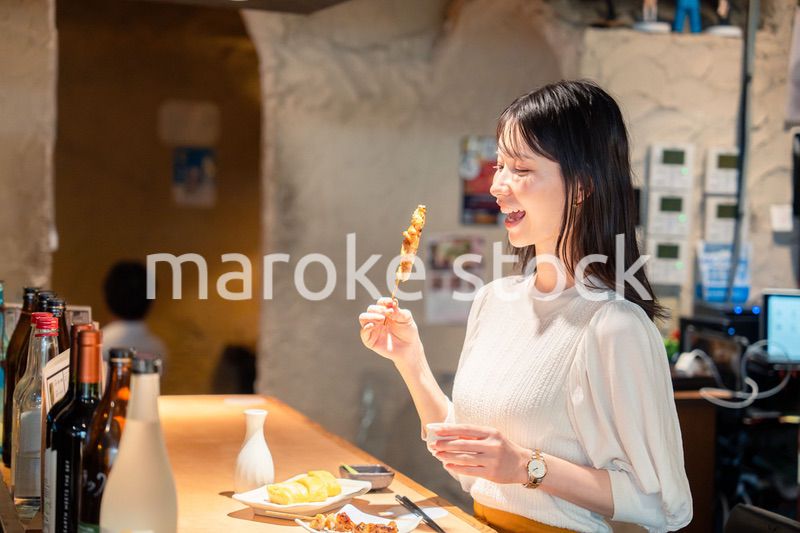一人でカウンター席に座って焼き鳥を食べる女性