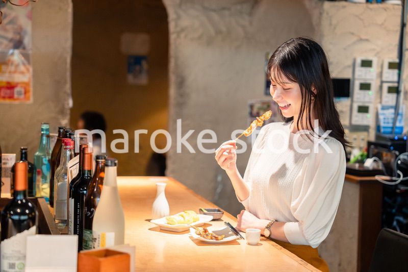一人でカウンター席に座って焼き鳥を食べる女性