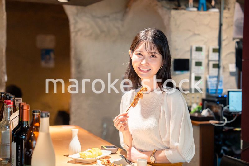 一人でカウンター席に座って焼き鳥を食べる女性